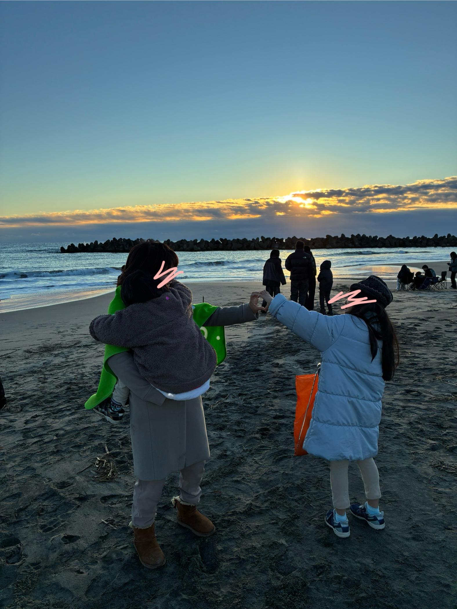 浜辺で子どもを抱っこした母親と娘が、手でハートを作っている